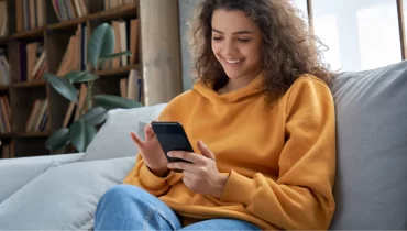 Mujer sonriendo revisando su smartphone sentada en el sofá para encontrar seguro médico