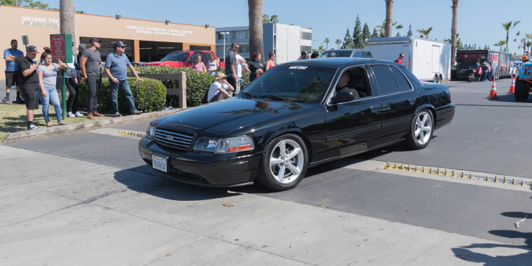 Ford Crown Victoria negro avanzando en la calle durante una exhibición de autos.