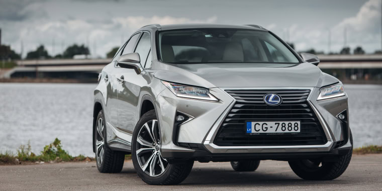 Lexus RX plateado estacionado frente a un río en un día nublado. 