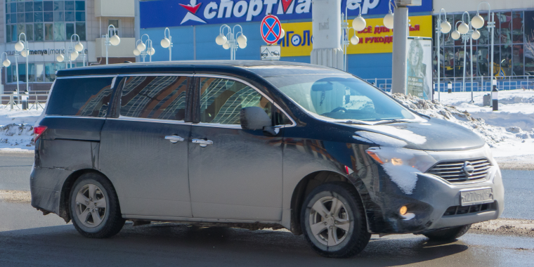 Nissan Quest azul avanzando en la carretera de una ciudad en un día nublado – Freeway, seguro de auto barato para la Nissan Quest. 
